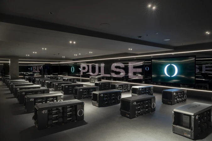 Fitness studio interior featuring rows of workout stations with weights, illuminated 'PULSE' text, and a modern, dark-themed design.