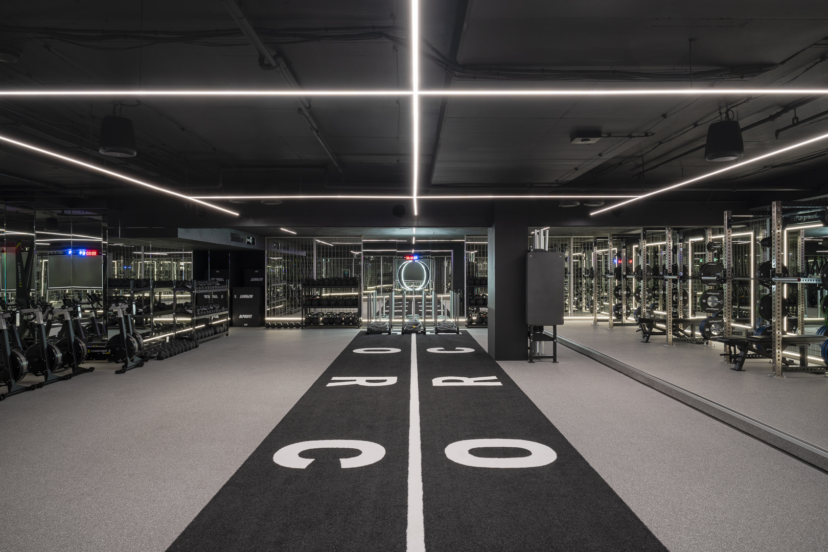 Symmetrical shot of a modern gym interior with rows of fitness equipment, mirrored walls, and a black track with white lettering.