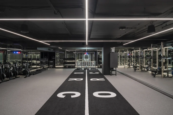 Symmetrical shot of a modern gym interior with rows of fitness equipment, mirrored walls, and a black track with white lettering.