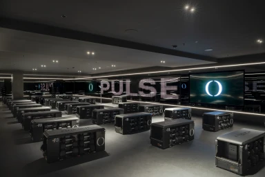 Modern dark fitness studio interior with rows of modular workout benches facing digital screens displaying the word PULSE.