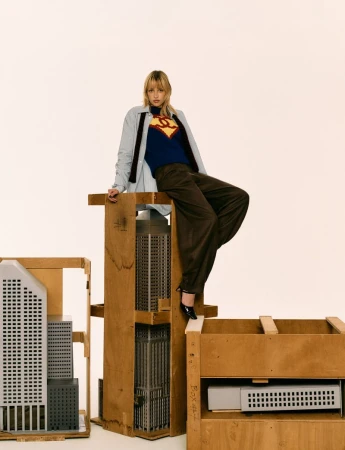 Angèle sits perched atop wooden architectural crates containing miniature skyscraper models against a plain white backdrop.