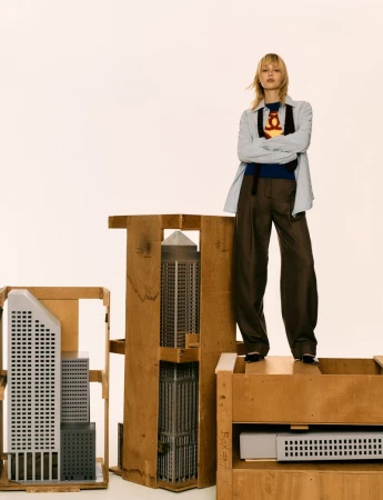 Singer Angèle stands atop wooden shipping crates housing miniature skyscraper models against a seamless white studio backdrop.