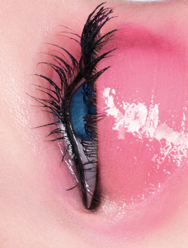 Extreme macro close-up of an eye featuring glossy pink eyeshadow, dramatic spiky black eyelashes, and a blue iris.
