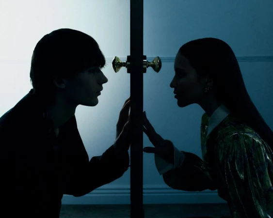 Profile silhouettes of a young man and woman placing their hands against opposite sides of a doorway under cool blue light.