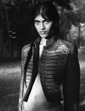 Monochrome portrait of model Ashley Radjarame wearing an embroidered open military jacket in a wooded outdoor setting.