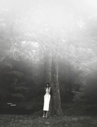 Model Ashley Radjarame standing against a large tree in a misty forest for Numero Netherlands Soft Remains