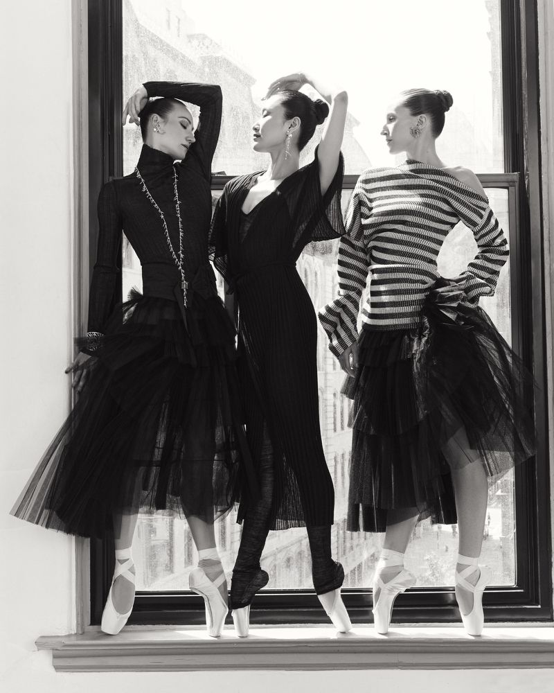 Three ballerinas in pointe shoes and tulle skirts pose in front of a bright window, dressed in black and white, shot in black and white.