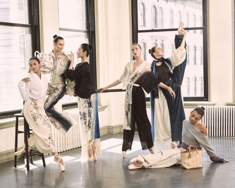 Group of ballet dancers in floral patterned outfits strike poses in a dance studio near large windows, exuding elegance and poise.