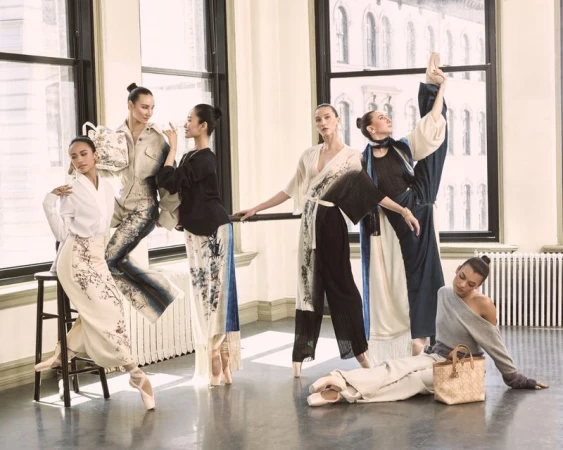 Group of ballet dancers in floral patterned outfits strike poses in a dance studio near large windows, exuding elegance and poise.