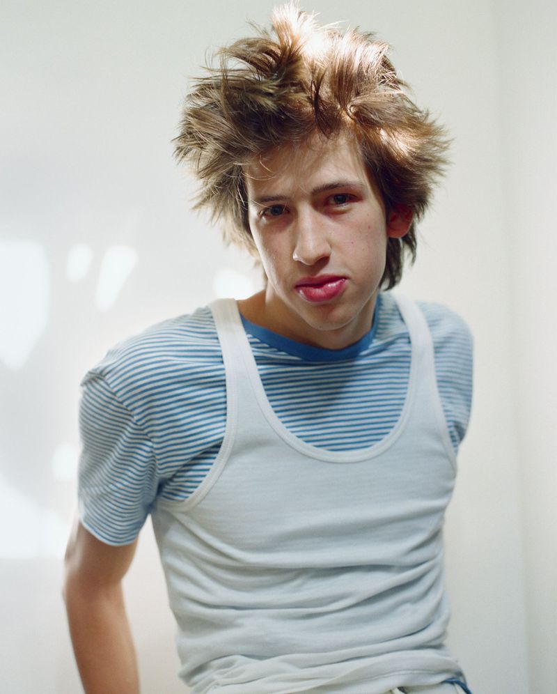 Model Elan Lee wearing a white tank top layered over a blue striped t-shirt against a white studio wall.