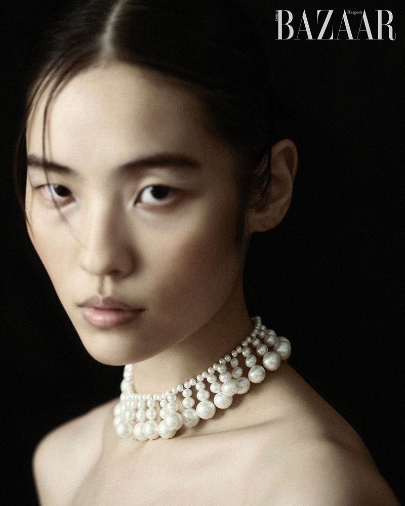 Portrait of an Asian woman wearing a pearl choker necklace, gazing directly at the camera against a dark background in a photo studio.