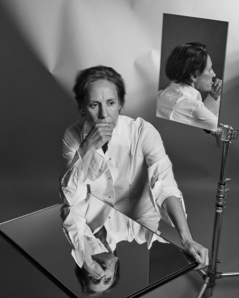 Black and white portrait of Fiona Shaw wearing a white collared shirt, posed with reflection mirrors in a studio setting.