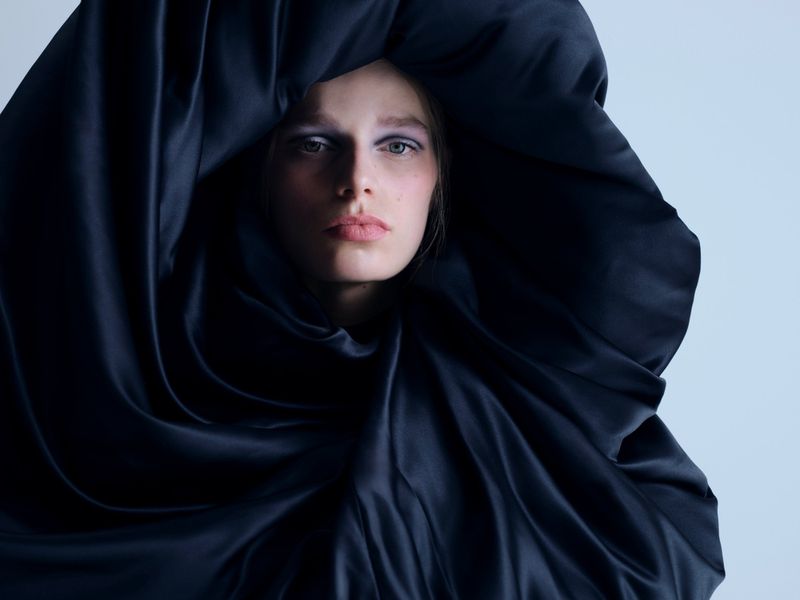 Model Saar Mansvelt Beck framed by voluminous draped black satin fabric against a pale studio backdrop.