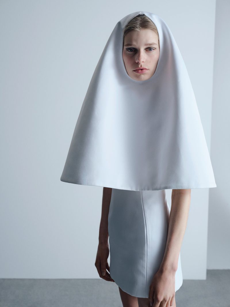 Model Saar Mansvelt Beck wearing a sculptural white conical hood piece and matching structured mini dress in a studio.