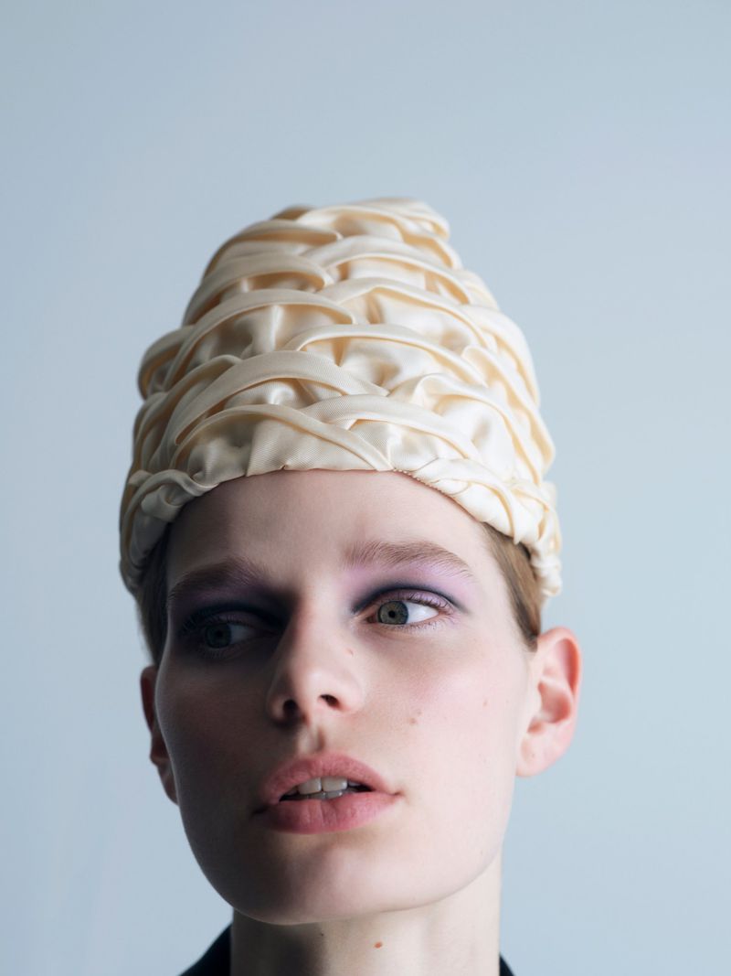 Close-up of model Saar Mansvelt Beck wearing an intricate cream woven satin headpiece against a plain pale backdrop.