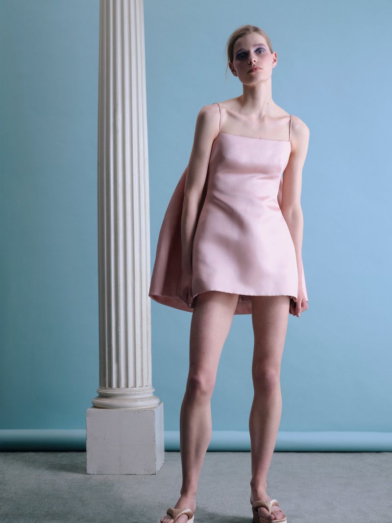 Model in pink minidress standing beside a white classical column against a blue background for Beyond Noise