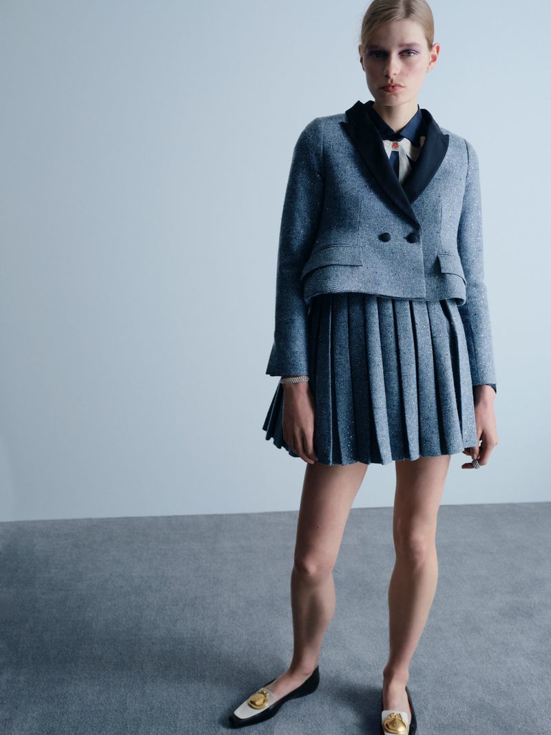 Model Saar Mansvelt Beck posing in a grey cropped jacket and matching pleated mini skirt with two-tone loafers in a studio.