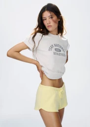 Model Mahalia Henderson posing in an off-white graphic t-shirt and yellow drawstring sweat shorts against a white studio backdrop.