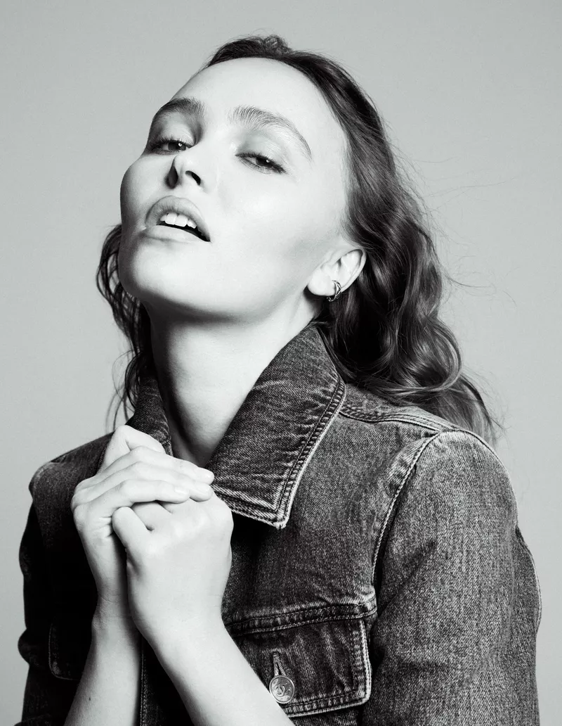 Black and white portrait of Lily-Rose Depp posing in a denim jacket with hands near her collar.