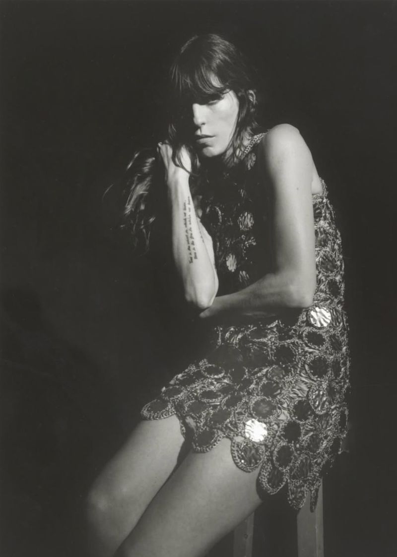 Lou Doillon seated in an embellished circular chainmail mini dress against a dark backdrop in black and white.