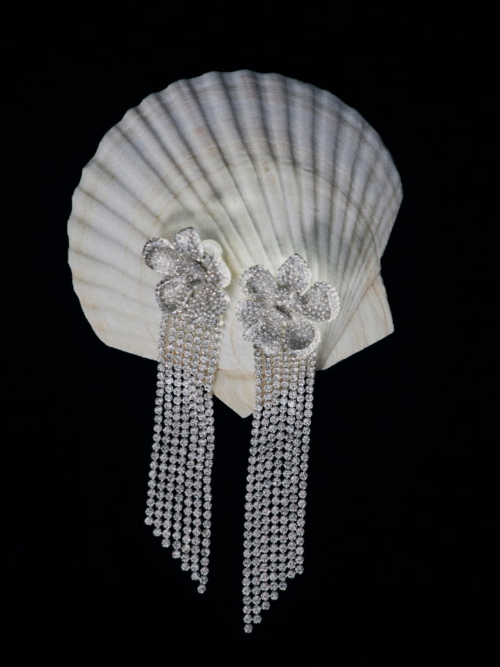 Elegant dangle earrings with floral design displayed on a seashell against a black background for a luxurious jewelry showcase.