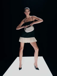 Model in black dress and ruffled skirt standing on an illuminated platform against a dark background, holding a small handbag