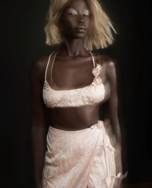 Striking fashion portrait of a woman with blonde hair in a pink two-piece outfit against a dark background in a studio setting.