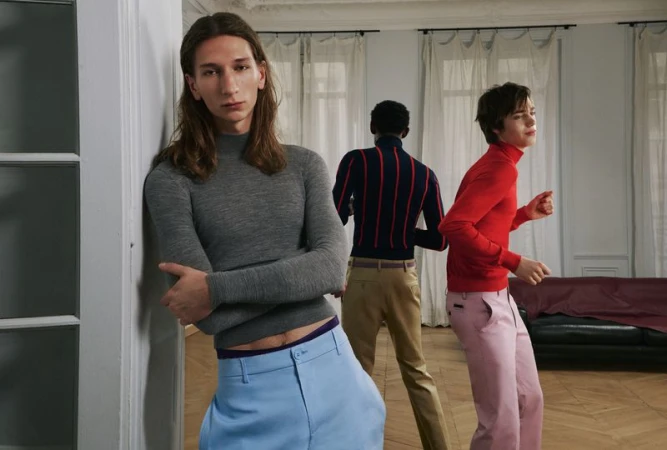 Three male models in an apartment interior wearing colourful turtlenecks and trousers for AnOther Man Magazine.