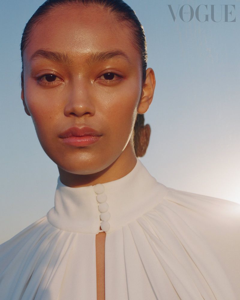 Close-up portrait of model Aneken Zaldivar wearing a high-neck white pleated dress against a clear sky for Vogue Mexico.