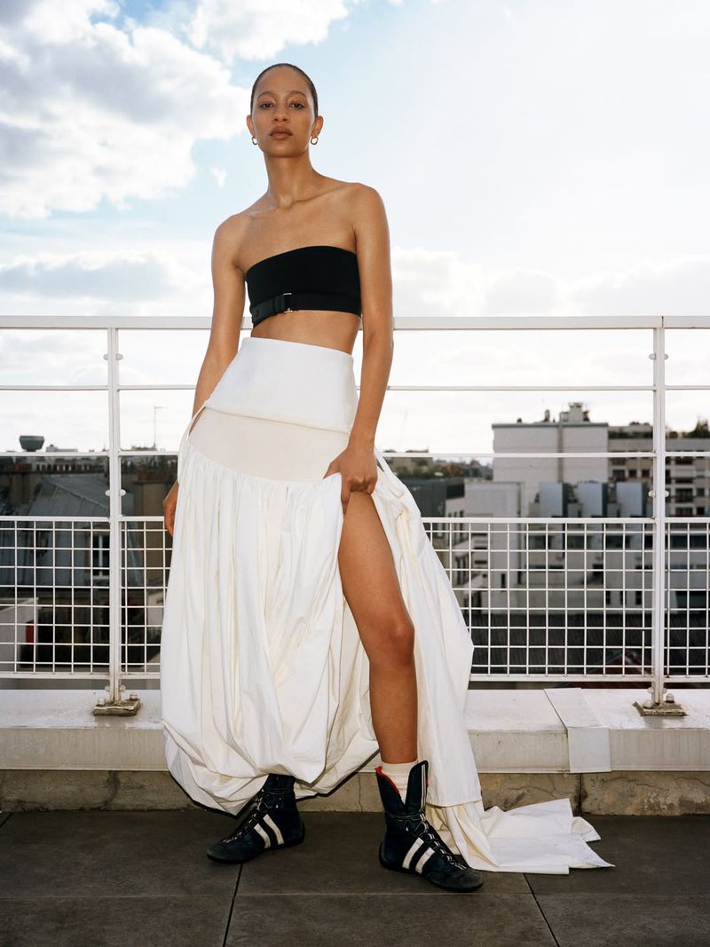 Selena Forrest posing on a rooftop wearing a black bandeau top, voluminous white slit skirt, and black high-top sneakers.