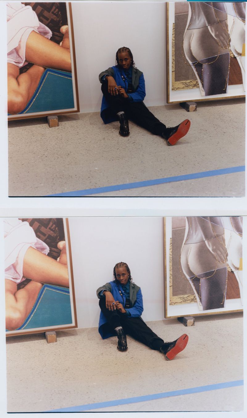 Person sits between two framed art images, one with legs and one with a partially visible butt, in an indoor art gallery or studio setting.