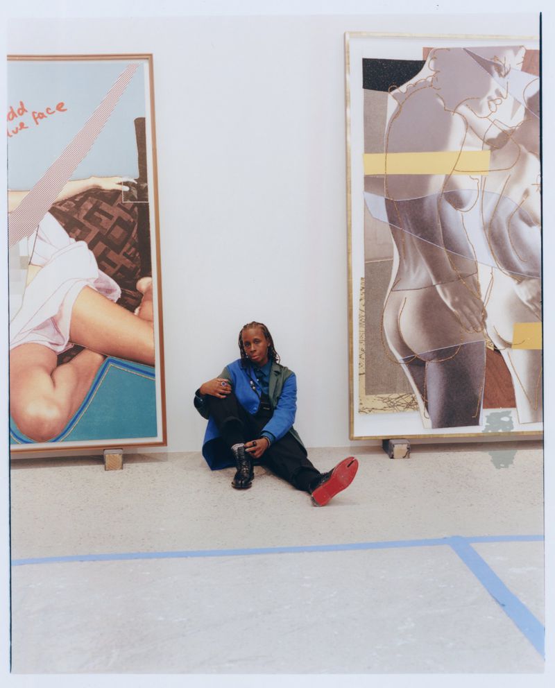 Artist seated on the floor between two large framed artworks in a gallery setting.