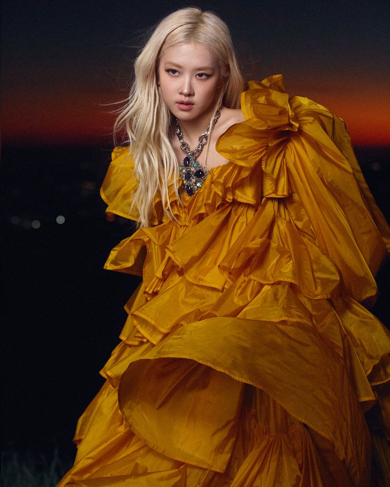 Rosé wearing a voluminous ruffled yellow gown and statement necklace against a twilight sky for CR Fashion Book.