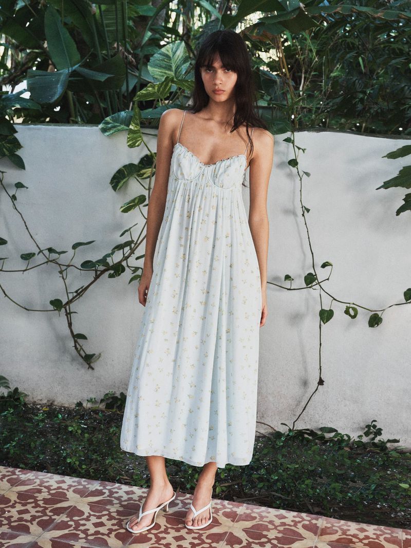 Clara Marques models a white floral spaghetti-strap sundress with white heeled thong sandals in an Aritzia fashion campaign.
