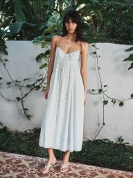 Clara Marques models a white floral spaghetti-strap sundress with white heeled thong sandals in an Aritzia fashion campaign.
