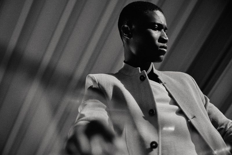 Black and white low-angle portrait of model Kwaku Ansong wearing a structured buttoned jacket for Paul Stuart.