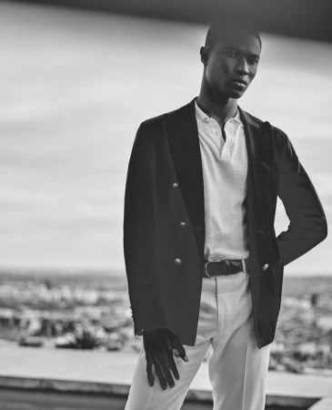 Monochrome portrait of model Kwaku Ansong wearing a double-breasted blazer, polo shirt, and light trousers outdoors.
