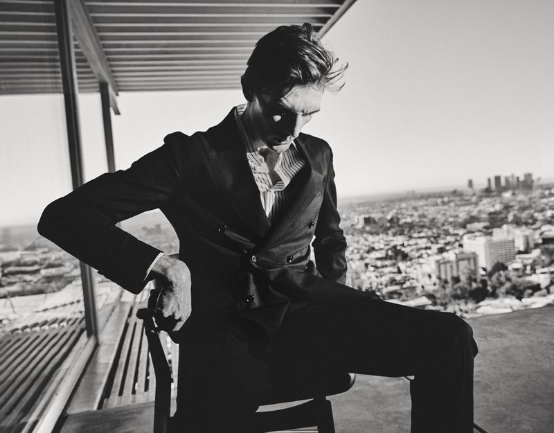 Model Finnlay Davis wearing a dark double-breasted suit seated before an expansive city skyline in a black and white portrait.