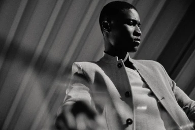 Black and white low-angle portrait of model Kwaku Ansong wearing a structured buttoned jacket for Paul Stuart.