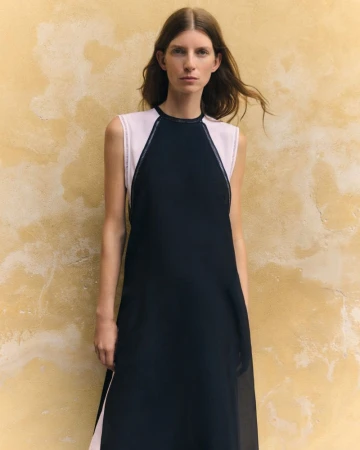 Model wearing a black and pale pink dress standing against a mottled yellow textured wall for Giada SS 2026 leisure collection.