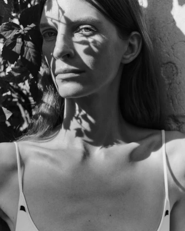 Black and white portrait of Luca Gajdus with leaf shadows across her face wearing a white spaghetti strap top.
