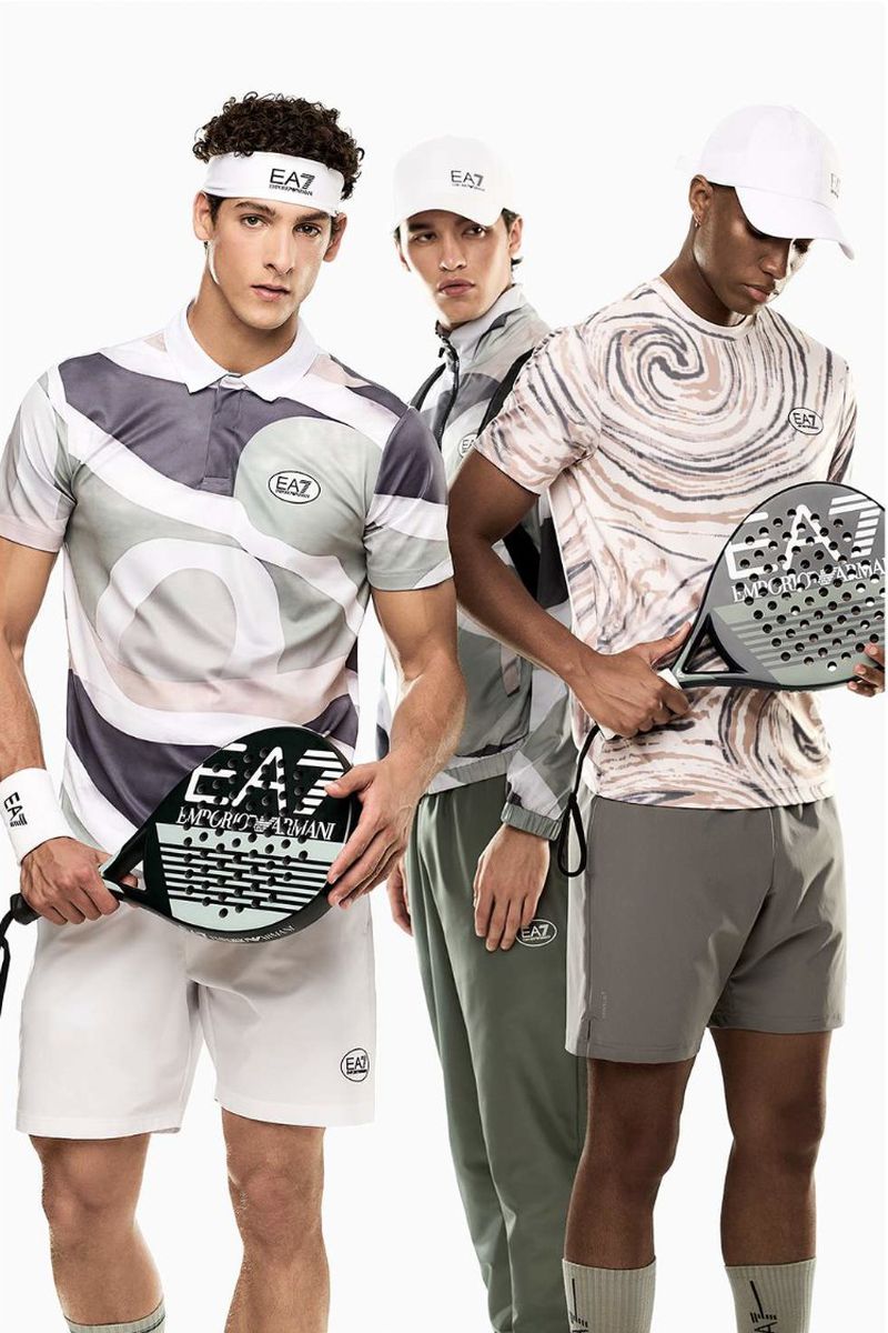 Three male models posing in EA7 Emporio Armani sportswear and holding padel rackets against a white background.