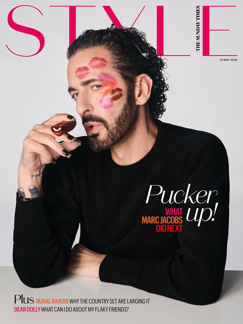 Magazine cover featuring adult male with dark hair, makeup kiss prints, and holding lipstick, against a light background with bold typography.
