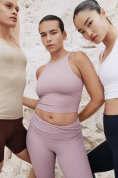 Three models wearing pastel and neutral athletic tops and leggings posed against a pale rocky cliff.