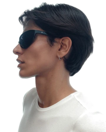 Profile portrait of a person with short dark hair wearing black sunglasses and a white t-shirt against a white background.