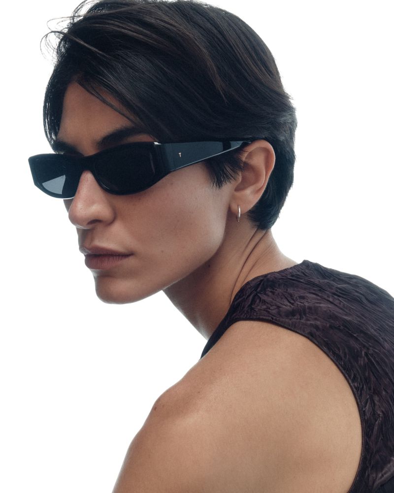 Close-up profile of a model wearing black angular sunglasses and a sleeveless crinkled top against a white background.