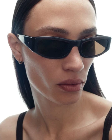 Close-up portrait of a model wearing black rectangular sunglasses and a black tank top against a bright white background.
