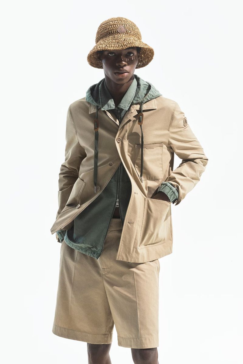 Model Zaram Obasi in a straw bucket hat, beige utility jacket, and matching shorts against a white studio background for Moncler.