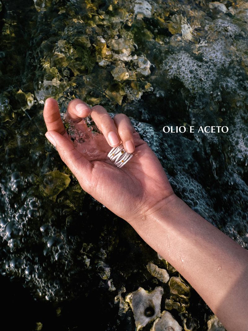 A hand wearing a multi-band wrap ring with amber stone accents resting over wet, barnacle-covered coastal rocks.