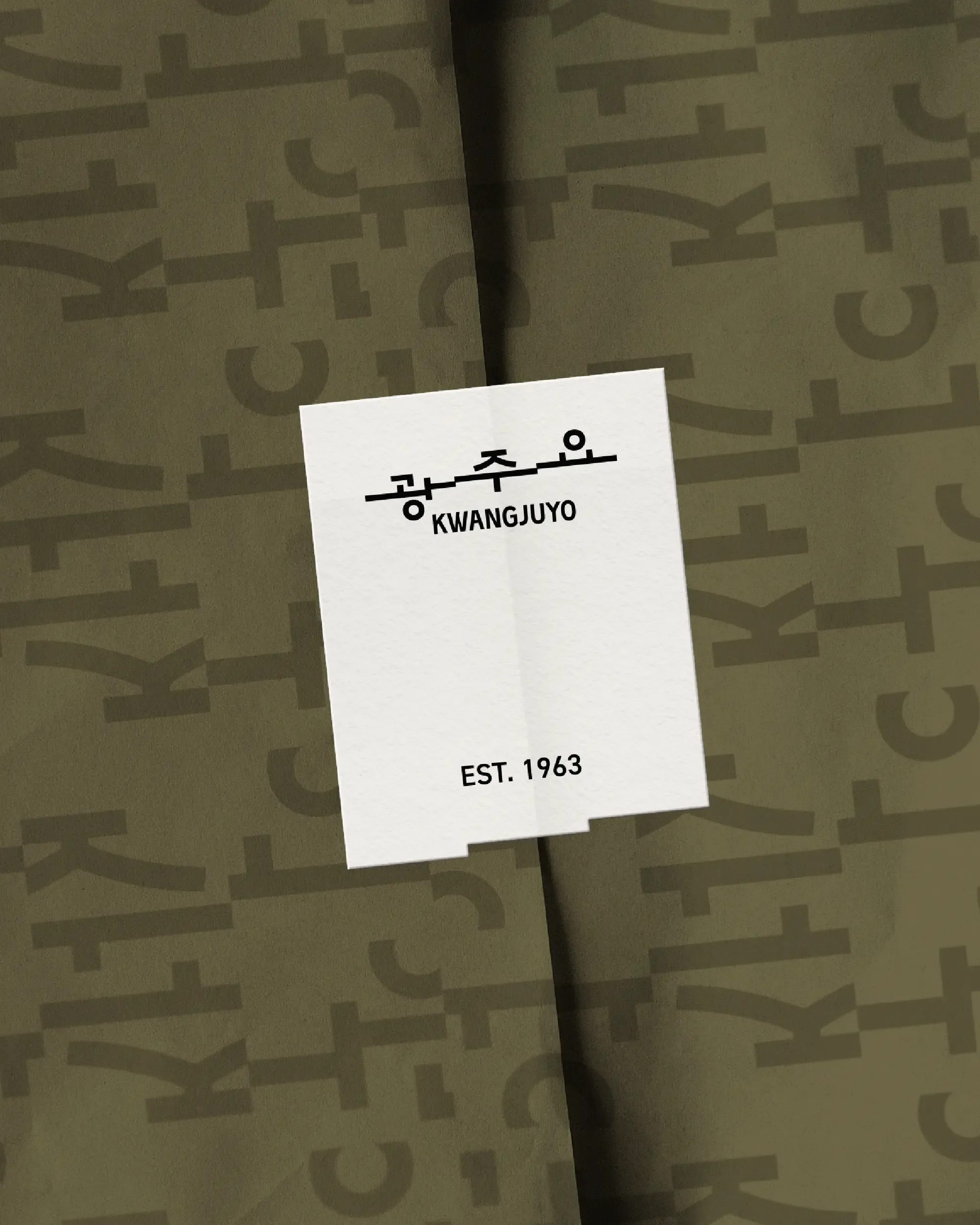 A white rectangular Kwangjuyo brand sticker sealing olive green wrapping paper printed with a Hangul typography pattern.